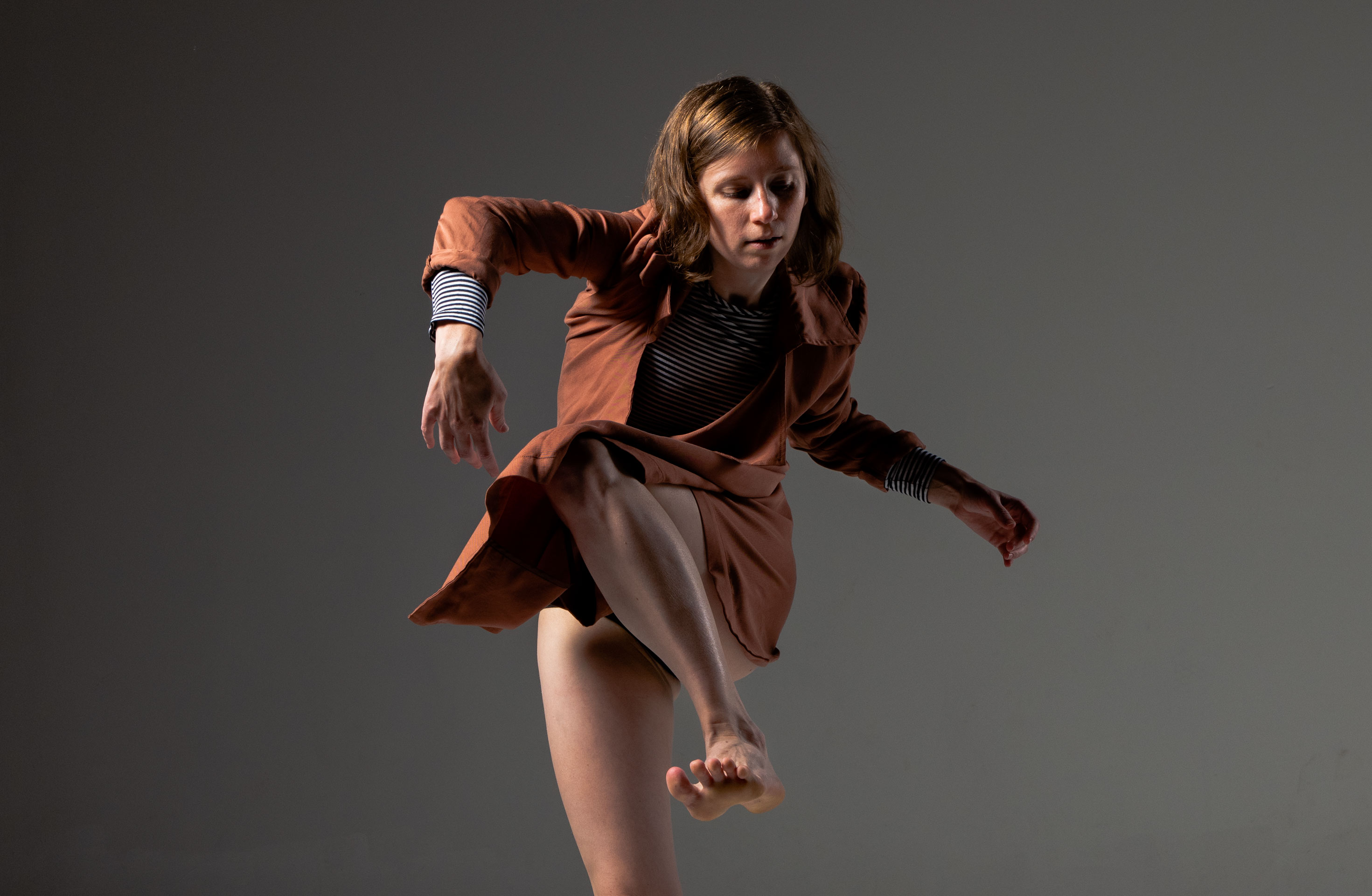 push/FOLD dancer Briley Jozwiak lifts up a gestural leg in an orange jacket at Cobalt Studios in Portland, Oregon | Photography: Jingzi Zhao